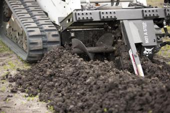 Bobcat trencher close-up trenching into black dirt.