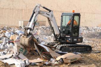Clamp (thumb) attachment on the Bobcat E45 compact excavator lifts rubbish in a waste facility.