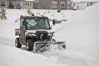 Bobcat 3650 UTV travels down a mountain road while using the snowblower attachment.