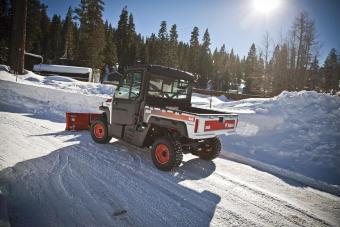 UTV with snow blade (snowblade) attachment pushes through fresh snow on a roadway.