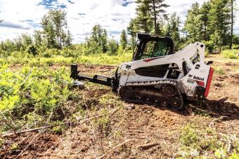 Bobcat brush saw (cutter) attachment is used to remove a tree in a wooded area.